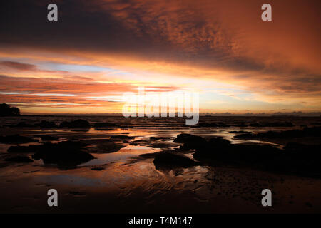 Sky con profonda appendere nubi e fango umido durante la bassa marea swathed in giallo e rosso brillante luce durante il tramonto su isola tropicale Ko Lanta, Th Foto Stock