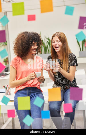 Giovane donna di affari con la fidanzata in ufficio sta godendo di un SMS sullo smartphone Foto Stock