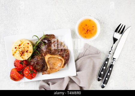 Preparate la bistecca di manzo osso bucco con purè di patate e pomodori sul tavolo bianco. Vista dall'alto. Spazio di copia Foto Stock