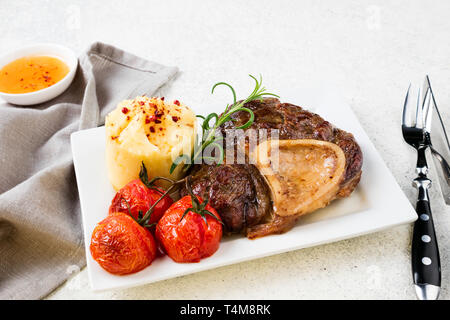 Preparate la bistecca di manzo osso bucco con purè di patate e pomodori sul tavolo bianco. Spazio di copia Foto Stock