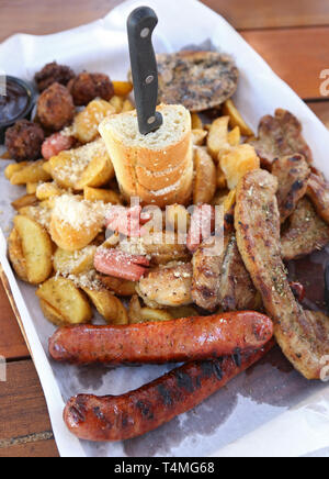 Grande lastra con una deliziosa varietà di carne - bistecca alla griglia, polpette di carne, pollo, salsicce e pane e patate fritte Foto Stock