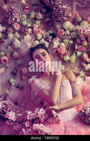 Delicatezza. Vista superiore della bella giovane donna in rosa ballet tutu circondato da fiori. La molla umore e tenerezza nella luce di corallo. Foto d'arte. Concetto di primavera sbocciano i fiori e la natura di risveglio. Foto Stock