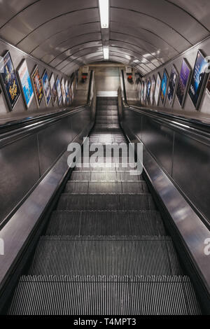 London, Regno Unito - 13 Aprile 2019: vista giù per la scala mobile che conduce alla piattaforma di Embankment stazione della metropolitana. La metropolitana di Londra è la più antica sotto Foto Stock