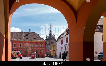 SIGHISOARA, ROMANIA - Aprile 9, 2019: La Torre dell Orologio in Sighisoara, visto attraverso gli archi presso l'ingresso in Piazza Cittadella in una giornata di sole. Foto Stock