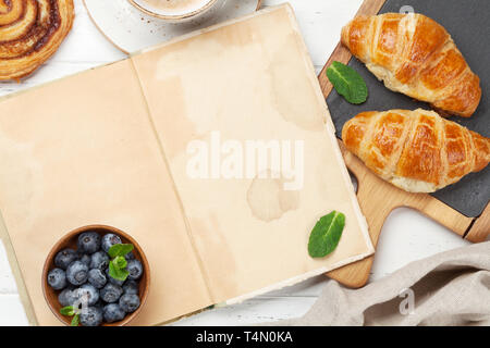 Caffè, cornetti, panini alla cannella e le bacche di prima colazione. Su un tavolo di legno. Vista da sopra con le pagine del libro per il testo Foto Stock