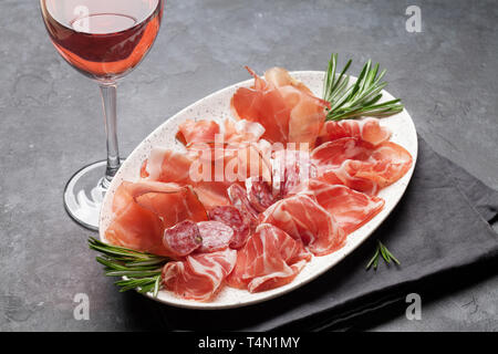 Tradizionale spagnolo jamon, prosciutto crudo, salame, prosciutto di Parma.  Piastra di antipasto e un bicchiere di vino Foto stock - Alamy
