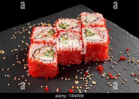 Uramaki sushi servita sulla pietra nera piastra, decorata con sesamo. California roll riempita con il cetriolo, la crema di formaggio e di carne di granchio, coperto con tobiko roe. Foto Stock