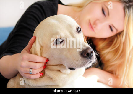 La donna con il cane è a riposo nel letto di casa, rilassante nella camera da letto. Ragazza è petting con il suo cane. Ritratto di giallo simpatico Labrador retriever e il suo proprietario. Foto Stock