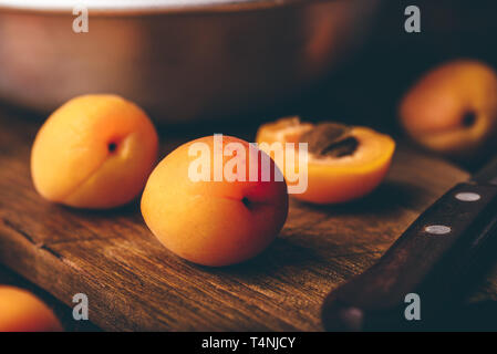 Mellow albicocche con il coltello su un vecchio tagliere di legno e metallo ciotola con frutti Foto Stock