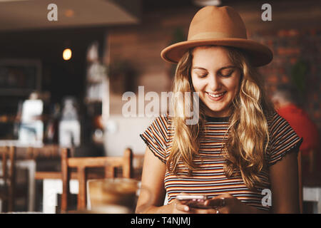 Attraente giovane femmina chattare su mobile al cafe Foto Stock