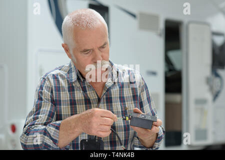 Senior uomo esaminando adattatore elettrico al di fuori il suo motorhome Foto Stock