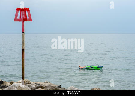 Un uomo che si gode il tempo caldo in una barca gonfiabile lungo la spiaggia di Highcliffe a Dorset, Inghilterra, Regno Unito. Foto Stock