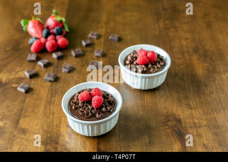 Un decadente Mousse al cioccolato Torta con glassa al cioccolato e guarnita con lamponi, more e riccioli di cioccolato su una tavola di legno in un ramekin dis Foto Stock