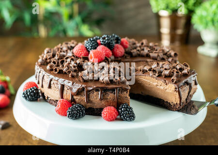 Un decadente Mousse al cioccolato Torta con glassa al cioccolato e guarnita con lamponi, more e riccioli di cioccolato su una tavola di legno Foto Stock