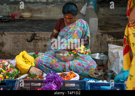 Posizione orizzontale ritratto di una donna in un duro lavoro rendendo ghirlande a Mattuthavani mercato dei fiori a Madurai, India. Foto Stock