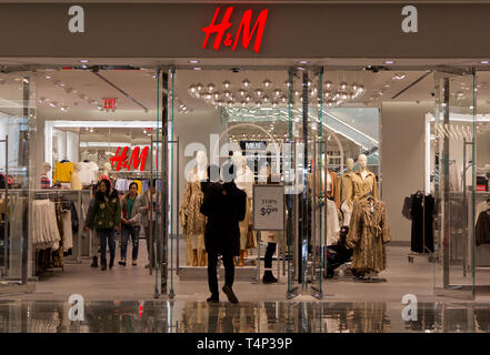 Vista posteriore del semi-stagliano uomo che porta il toddler boy, passeggiate in H&M negozio di abbigliamento/store presso il centro commerciale di nuovi cantieri Hudson complesso che aveva aperto in precedenza che mese, altamente riflettente piano al di fuori della porta sotto i suoi piedi, mentre gli amanti dello shopping all'interno di sfoglia o a piedi verso l'uscita. Cantieri di Hudson, New York il nuovissimo quartiere, ha debuttato il 15 marzo 2019, a controversie circa il fatto che esso era troppo elitario. Secondo una azienda Press release, lo sviluppo "riunisce per la prima volta il lato ovest e i vicini quartieri di Chelsea e Hell's Kitchen". Foto Stock