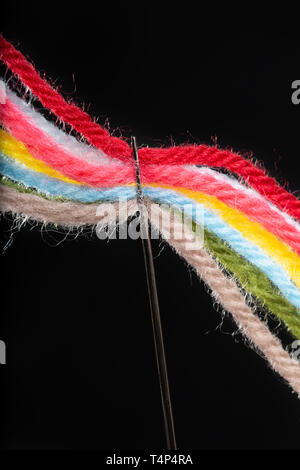 Su uno sfondo nero, più luminoso multicolore di fili di lana sono passano attraverso la cruna dell'ago. Close-up Foto Stock