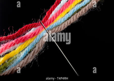 Su uno sfondo nero, più luminoso multicolore di fili di lana sono passano attraverso la cruna dell'ago. Close-up Foto Stock