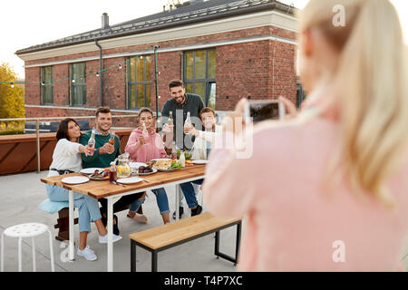 Tempo libero e concetto di persone - happy amici con bevande analcoliche aventi il barbecue sul tetto in estate e fotografando tramite smartphone Foto Stock