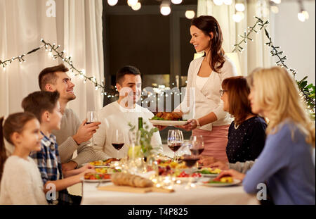 Celebrazione, vacanze e concetto di persone - donna felice offre pollo arrosto alla famiglia avente cena a casa Foto Stock