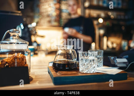 Occhiali con caffè nero e acqua filtrata, maschio barista presso il cafe o banco bar sullo sfondo. Professional preparazione espresso da barista in CAF Foto Stock