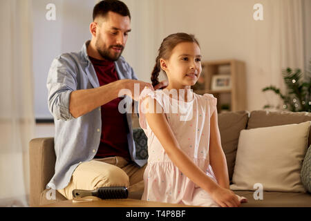 La famiglia e il concetto di persone - happy padre figlia di intrecciatura capelli a casa di sera Foto Stock