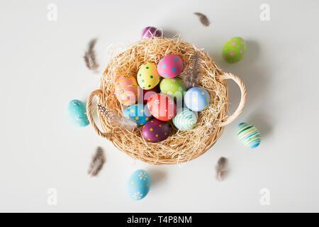 Pasqua, vacanze e concetto di tradizione - uova colorate in cesto con paglia e quaglie piume su sfondo bianco Foto Stock