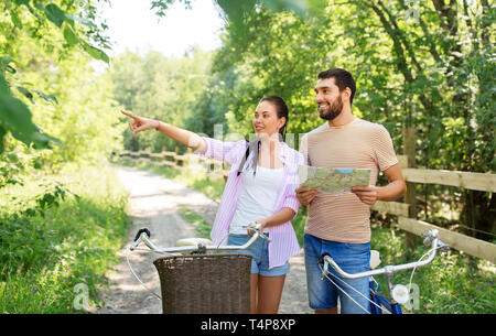 Viaggio, viaggio, il tempo libero e il concetto di stile di vita - felice coppia giovane con mappa e biciclette alla ricerca di posizione in paese in estate Foto Stock