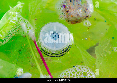 Utilizzate il cestino in borsa. Immondizia di plastica essendo posti in acqua glitter con accartocciata sacchetti verde Foto Stock