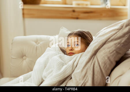 Una ragazza malata nel letto. Piccolo dolce piuttosto male i capelli castani ragazza con un freddo che giace nel letto avvolto in una calda coperta Foto Stock