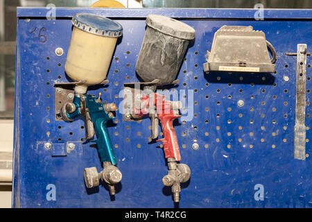 Due vernice corpo spruzzatore a pistola di rosso e di blu installato su un banco in un veicolo officina accanto a un altro strumento e lampada. Industria in auto service Foto Stock