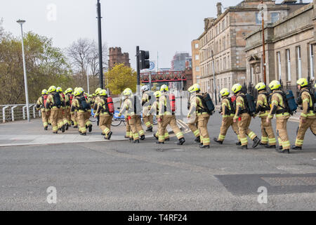 Glasgow, Scotland, Regno Unito. 18 Aprile, 2019. Sessanta partecipante vigili del fuoco piena di indossare un equipaggiamento protettivo personale su un sponsorizzato da marzo a raccogliere fondi per beneficenza a seguito di una heritage trail attraverso le strade della città. Il nuovo sono i vigili del fuoco in base alla scozzese del fuoco e di salvataggio Service National Training Center in Cambuslang, South Lanarkshire e sono undici settimane in formazione. Credito: Berretto Alamy/Live News Foto Stock