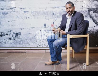 Mauer, Germania. Xvii Apr, 2019. John Ehret, sindaco del comune di Mauer, si siede di fronte a una grande foto in formato di Homo Heidelbergensis la ganascia inferiore trovata in Mauer in Grafenrain buca di sabbia di fronte a una replica del sito nella buca di sabbia. Questa ganascia ha un enorme significato per la storia dell'umanità. I fossili trovati in un luogo secco Neckar bow appartiene con i suoi 610 000 anni per i più antichi reperti umani in Europa. (A dpa 'Homo Heidelbergensis - La comunità che i sogni di un museo') Credito: Uwe Anspach/dpa/Alamy Live News Foto Stock