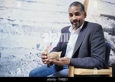 Mauer, Germania. Xvii Apr, 2019. John Ehret, sindaco del comune di Mauer, si siede di fronte a una grande foto in formato di Homo Heidelbergensis la ganascia inferiore trovata in Mauer in Grafenrain buca di sabbia di fronte a una replica del sito nella buca di sabbia. Questa ganascia ha un enorme significato per la storia dell'umanità. I fossili trovati in un luogo secco Neckar bow appartiene con i suoi 610 000 anni per i più antichi reperti umani in Europa. (A dpa 'Homo Heidelbergensis - La comunità che i sogni di un museo') Credito: Uwe Anspach/dpa/Alamy Live News Foto Stock