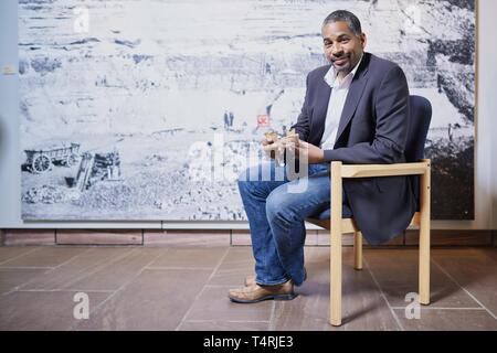 Mauer, Germania. Xvii Apr, 2019. John Ehret, sindaco del comune di Mauer, si siede di fronte a una grande foto in formato di Homo Heidelbergensis la ganascia inferiore trovata in Mauer in Grafenrain buca di sabbia di fronte a una replica del sito nella buca di sabbia. Questa ganascia ha un enorme significato per la storia dell'umanità. I fossili trovati in un luogo secco Neckar bow appartiene con i suoi 610 000 anni per i più antichi reperti umani in Europa. (A dpa 'Homo Heidelbergensis - La comunità che i sogni di un museo') Credito: Uwe Anspach/dpa/Alamy Live News Foto Stock