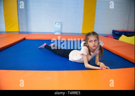 Cute sana slim bambina giacente sul trampolino per interni Foto Stock