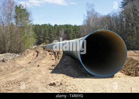 Grande concreta canalizzazione fognaria giacciono sul sito in costruzione nella foresta di primavera. Industriale paesaggio stagionali Foto Stock