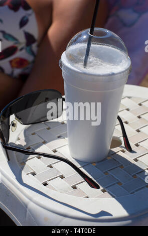 Caffè greco Frappé in tazza con schiuma nei pressi di occhiali da sole su sfondo sfocato parte del corpo della donna con il Bra Foto Stock