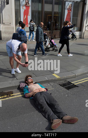 I passanti da guardare in giù su un giovane attivista in appoggio con la sua testa su un Oxford Circus frenare il giorno 4 di proteste da parte del cambiamento climatico attivisti ambientali con il gruppo di pressione la ribellione di estinzione, sul diciottesimo mese di aprile 2019, a Londra, in Inghilterra. Foto Stock