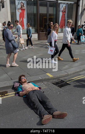 I passanti da guardare in giù su un giovane attivista in appoggio con la sua testa su un Oxford Circus frenare il giorno 4 di proteste da parte del cambiamento climatico attivisti ambientali con il gruppo di pressione la ribellione di estinzione, sul diciottesimo mese di aprile 2019, a Londra, in Inghilterra. Foto Stock