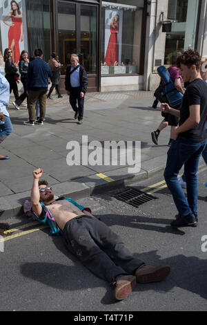 I passanti da guardare in giù su un giovane attivista in appoggio con la sua testa su un Oxford Circus frenare il giorno 4 di proteste da parte del cambiamento climatico attivisti ambientali con il gruppo di pressione la ribellione di estinzione, sul diciottesimo mese di aprile 2019, a Londra, in Inghilterra. Foto Stock