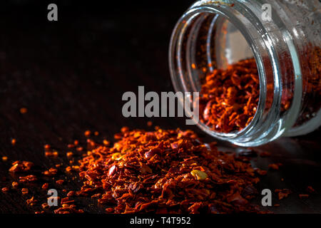 Close-up di fuoriuscite di chili fiocchi sul tavolo scuro Foto Stock