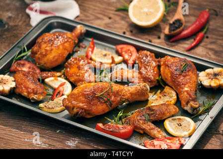 Il pollo al forno coscia e le ali sul vassoio da forno su legno scuro dello sfondo. Foto Stock