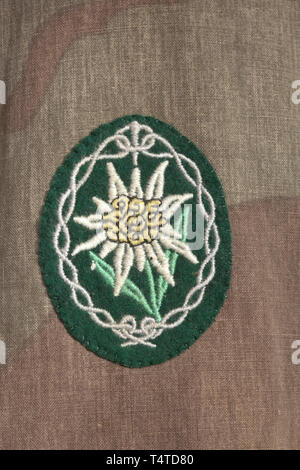 Un camuffamento pullover giacca per un Leutnant delle truppe di montagna professionnelle Feldfertigung aus einseitig bedrucktem, italienischem Zeltplanenstoff. Mittig ein zu 2/3 durchgehender Reißverschluss, einfacher Kragen, zwei aufgesetzte Brusttaschen mit Verschlussklappen, der untere Abschluss mit eingearbeiteter Zugschnur, die Ärmelenden durch Knöpfe verstellbar. Silberngestickter Brustadler, maschinengesticktes Ärmeledelweiß, aufgeschlaufte Schulterklappen. storica, storica, esercito, eserciti, forze armate, militare, militaria, oggetto, oggetti, alambicchi, clipping, ritagli, tagliare o, Editorial-Use-solo Foto Stock