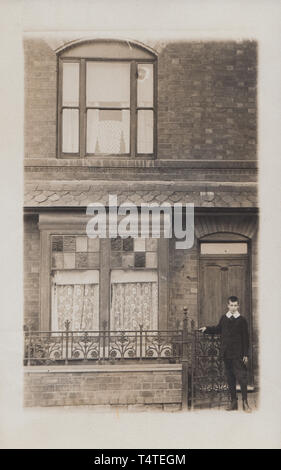 Vintage Cartolina fotografica che mostra una storica casa britannica con un ragazzo Edoardiano si fermò presso il cancello anteriore. Foto Stock