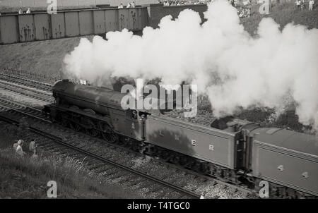 1969, storico su un ponte e un grassbank, guardare le persone come la mitica locomotiva a vapore, il Flying Scotsman', va passato, Inghilterra, Regno Unito. Foto Stock