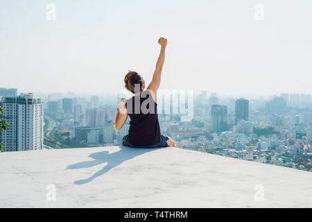 Uomo seduto sul tetto nero e mostra fino a mano con cielo blu di sfondo e sunshine,combattimenti uomo sul tetto Foto Stock