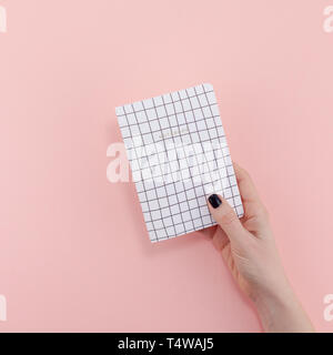 Vista superiore della donna mano con nero elegante manicure holding notepad con copia spazio sul colore rosa sfondo della carta in stile minimal. Modello per femin Foto Stock