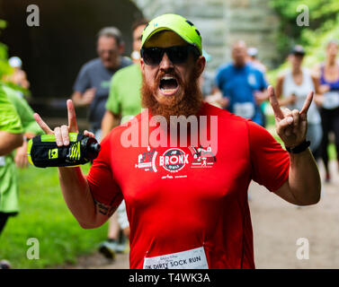 Babilonia, New York, USA - 12 agosto 2018: un runner racing a 10.000 metri di gara nel bosco diventa molto emozionato quando e pone per la fotocamera. Foto Stock