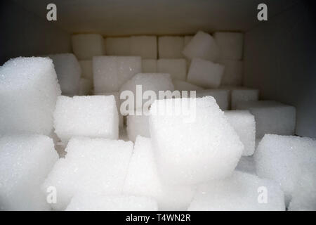 Macro shot di cubetti di zucchero accanto alla scatola di cartone sul tavolo di legno. Cibo malsano dolcificante, dolci cubetti di cristallo Foto Stock